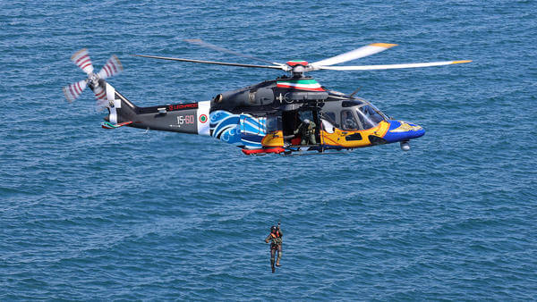 Helicopter flying over sea with paramedic hoisting out 