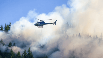 Helicopter dropping fire retardant over smokey trees