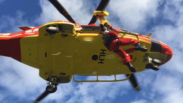 Air worker being lowered out of yellow and red helicopter